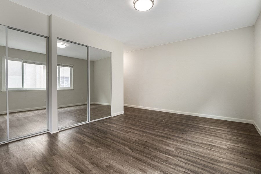 a bedroom with hardwood floors and a mirrored closet