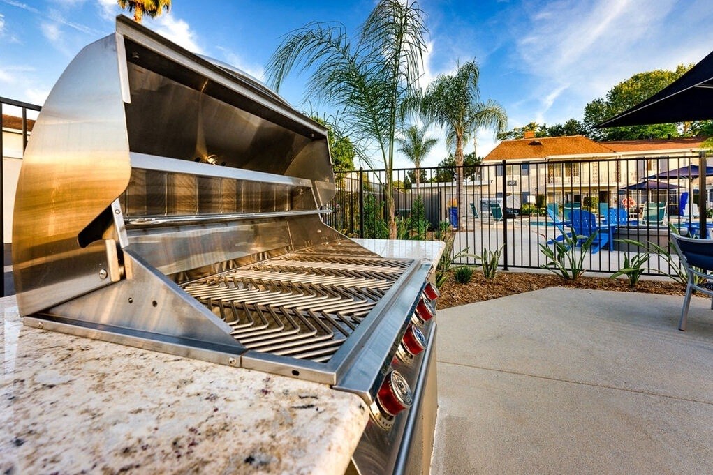 A large outdoor grill is in the foreground with a patio and pool in the background at Nola 624 Apartments, California, 91790