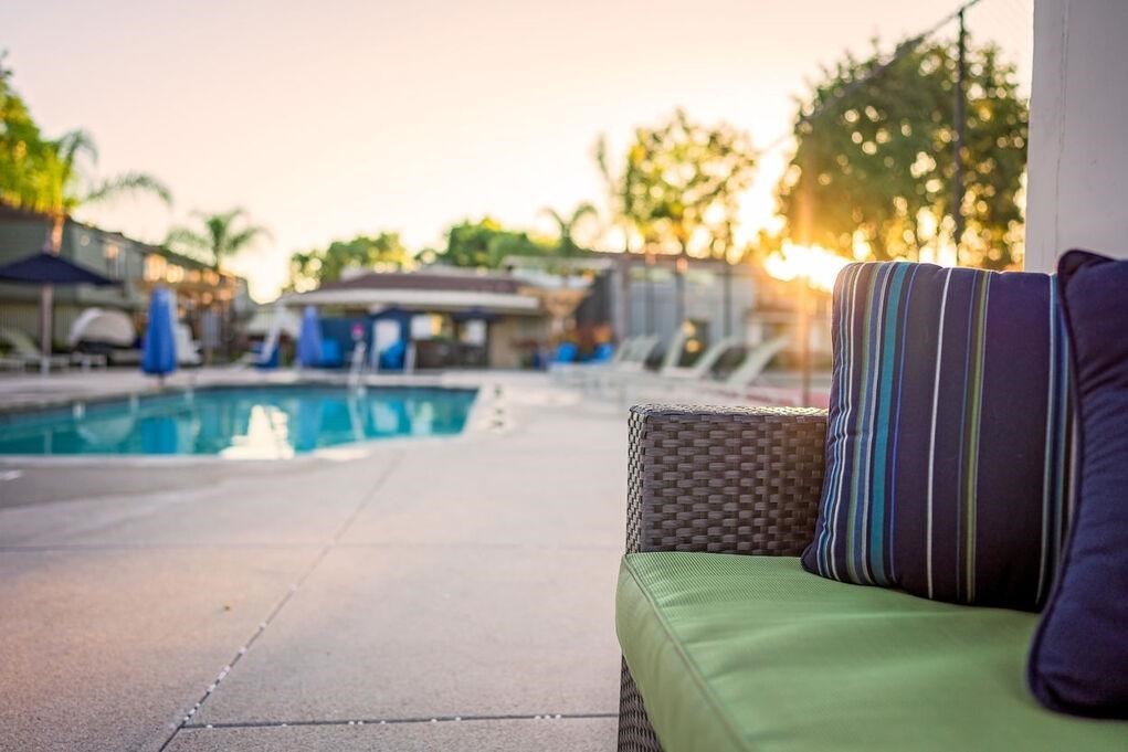 A poolside setting with a green couch and striped pillow at Nola 624 Apartments, West Covina, California