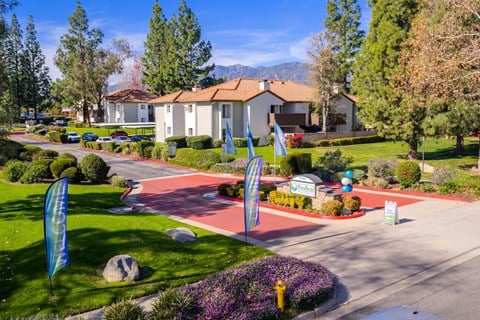 Community entrance with red brick driveway and banners at Woodbend Apartments, Alta Loma