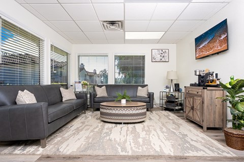 A living room with a grey couch, a coffee table, and a large window with blinds.