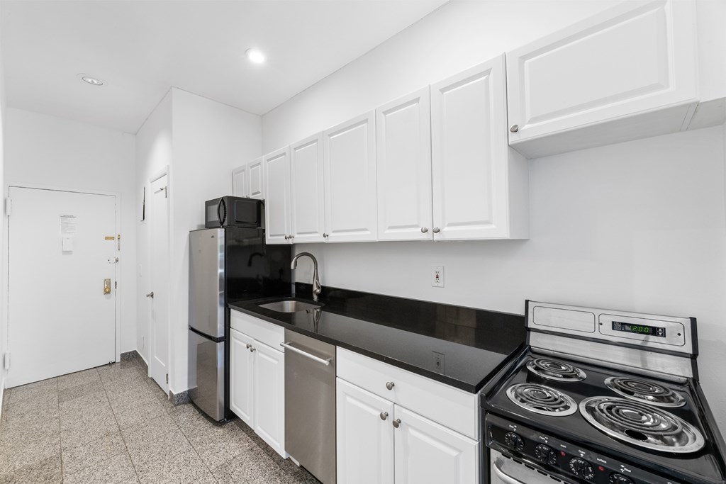 A kitchen with white cabinets and black countertops.