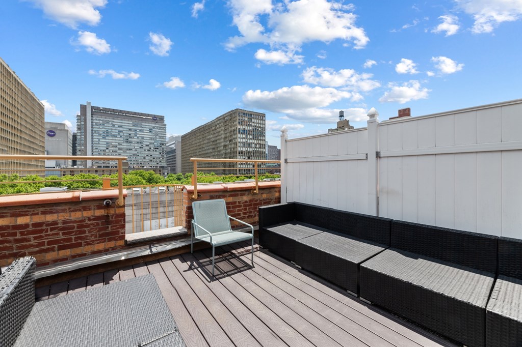 A wooden deck with a chair and a table in the foreground and a city skyline in the background.