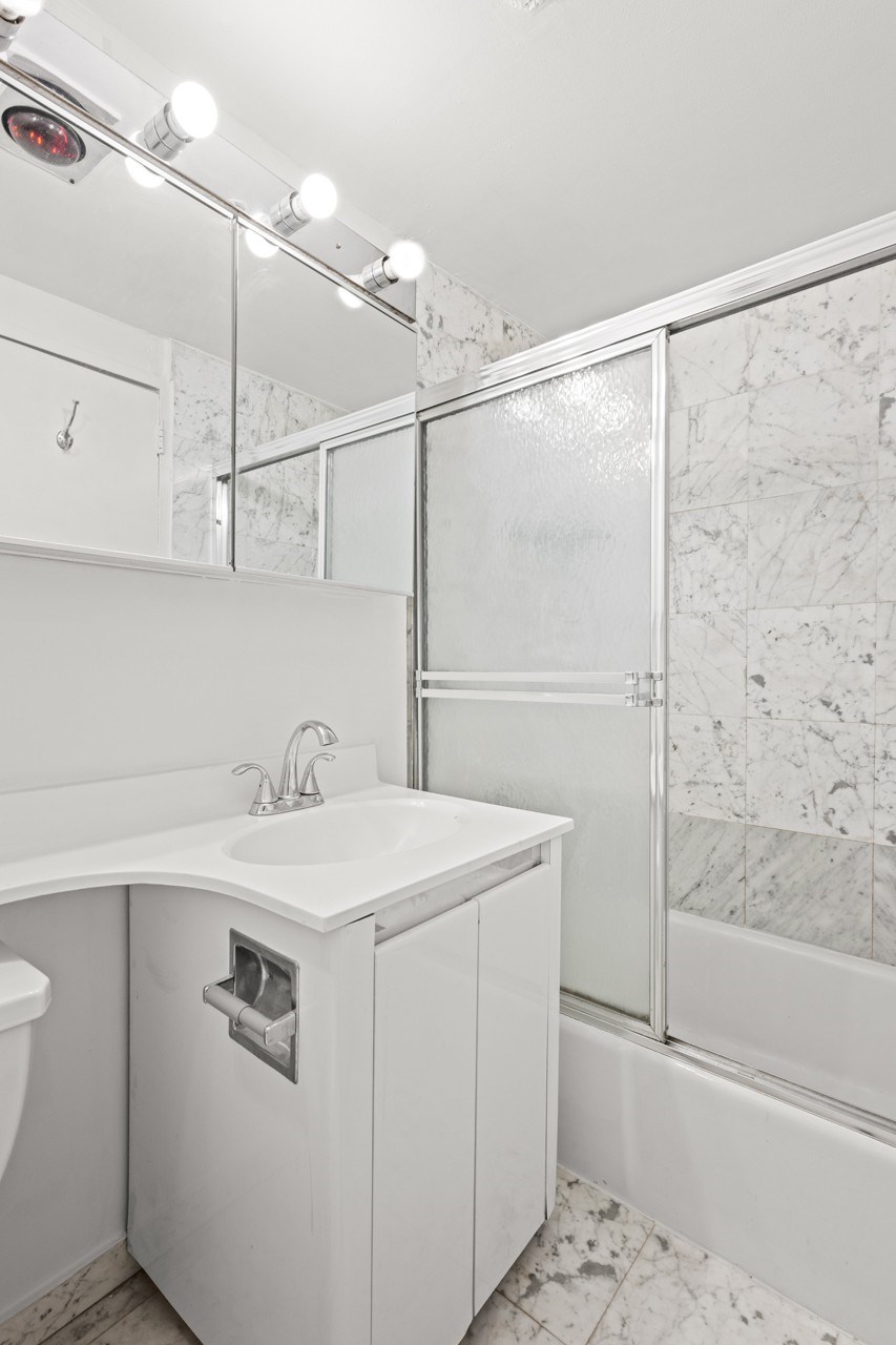 A white bathroom with a sink, mirror, and shower.