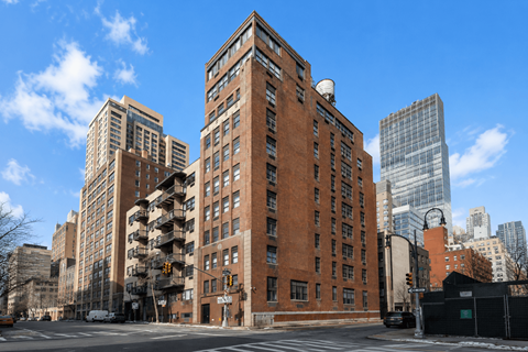 A large red brick building is in the middle of a city street.