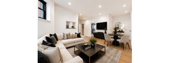 A modern living room with a white sofa, a black coffee table, and a TV mounted on the wall.