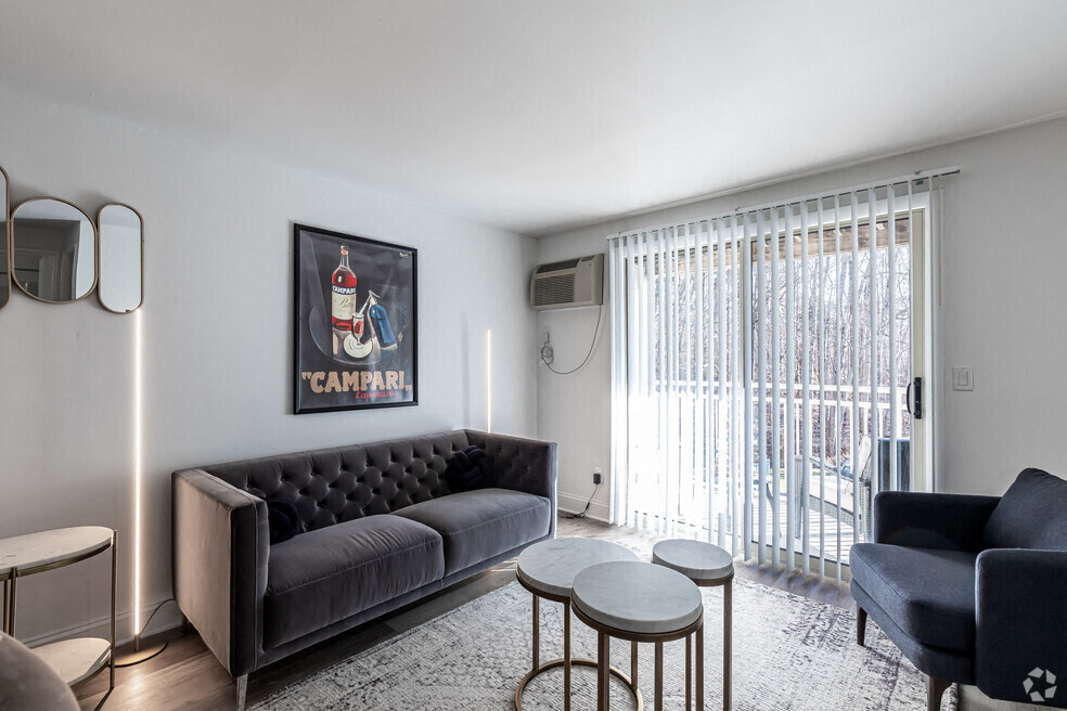 A living room with a black sofa, a grey armchair, a small table, and a framed picture on the wall.