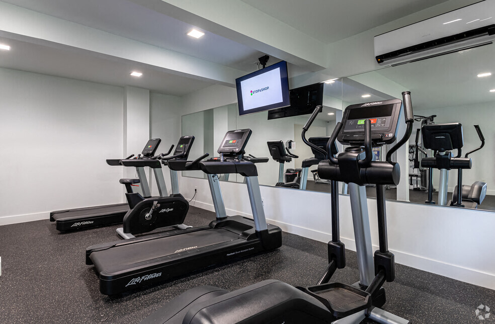 A gym with treadmills and a television mounted on the wall.