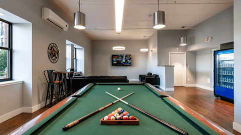 A pool table with a green felt cloth and a television mounted on the wall.