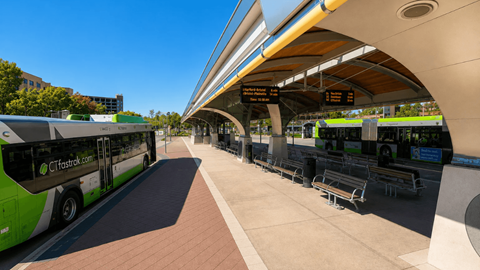 A bus station with a green and white bus and a yellow and white train in the background.