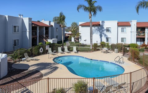 A pool surrounded by a fence and chairs in front of a white building.