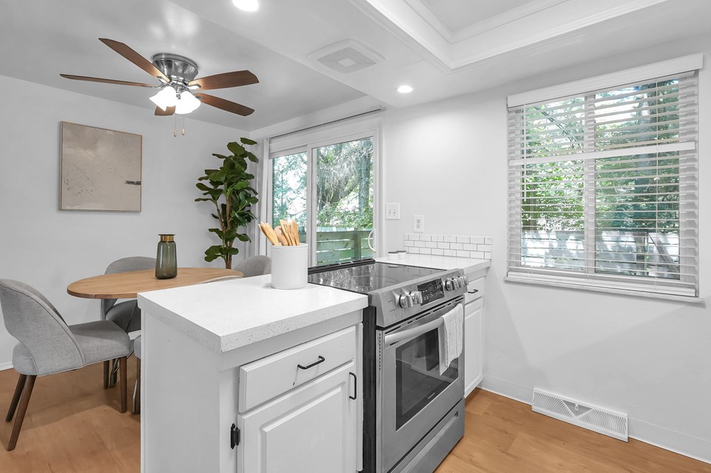 A modern kitchen with a white stove top oven and a fan ceiling light.