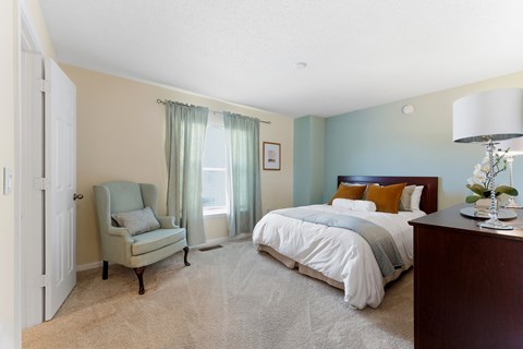 A bedroom with a bed, chair, and lamp.
