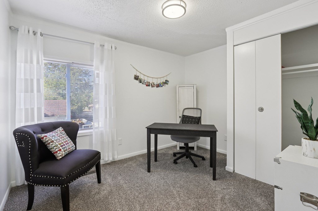 A room with a chair, desk, and a window with curtains.