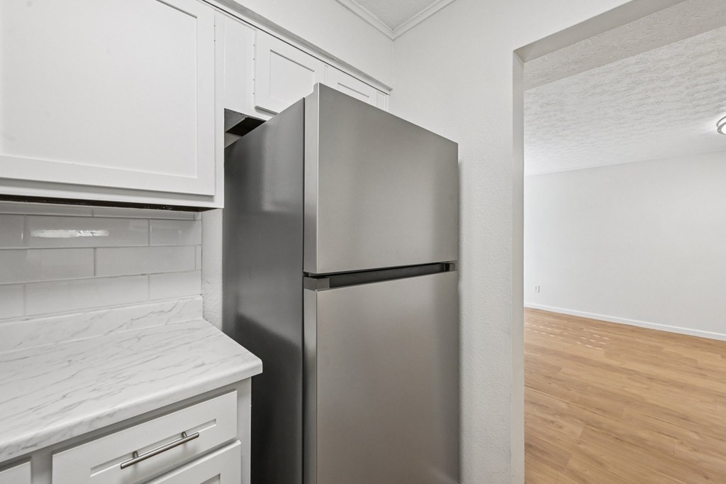 A stainless steel refrigerator stands in a kitchen with white cabinets.