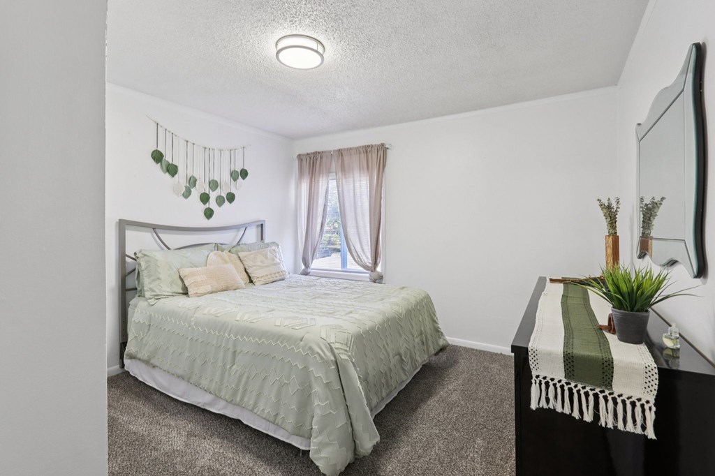 A bedroom with a bed, a nightstand, and a window.