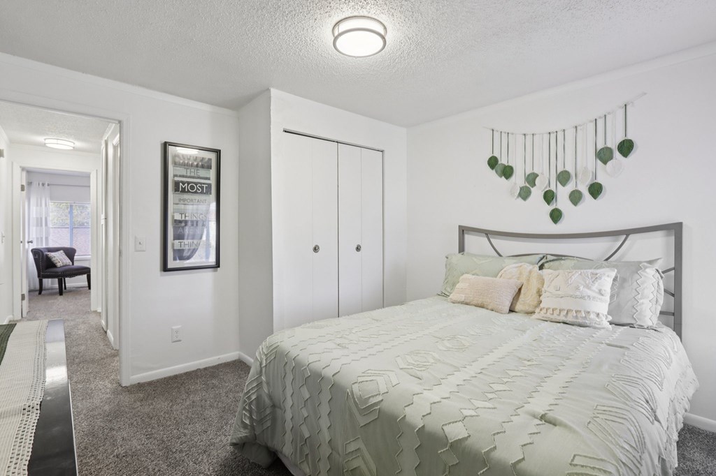 A bedroom with a bed, a chair, and a framed picture on the wall.