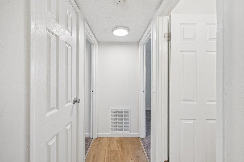 A hallway with white doors and a vent on the wall.