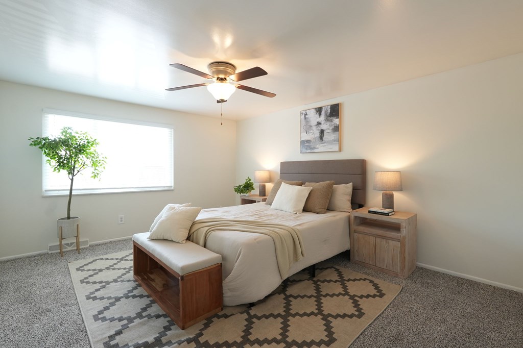 A bedroom with a bed, nightstand, and a plant.