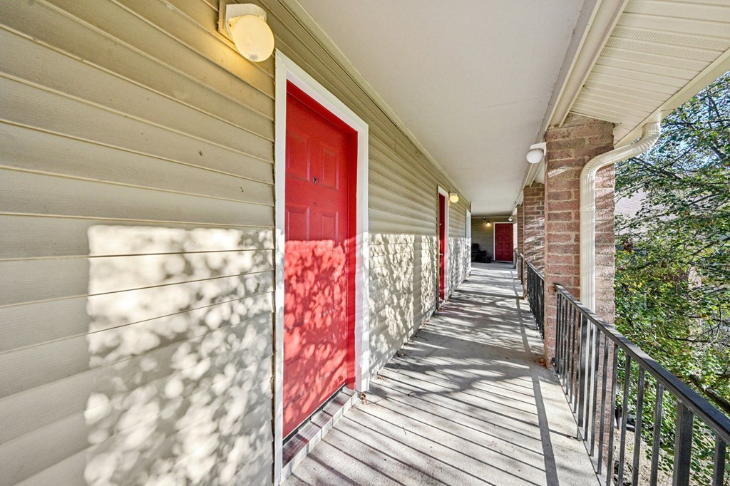 A red door is on the left side of a wooden deck.