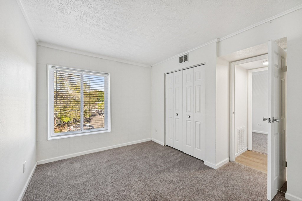 A room with a window, carpeted floor, and a white door.