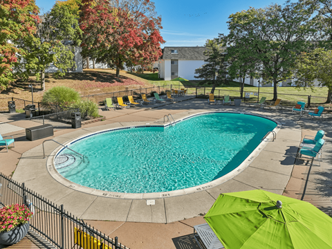 A green umbrella is open next to a swimming pool.