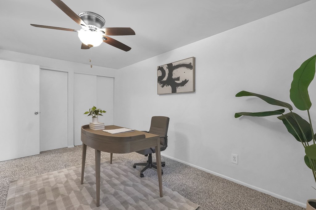 A room with a desk and a ceiling fan.