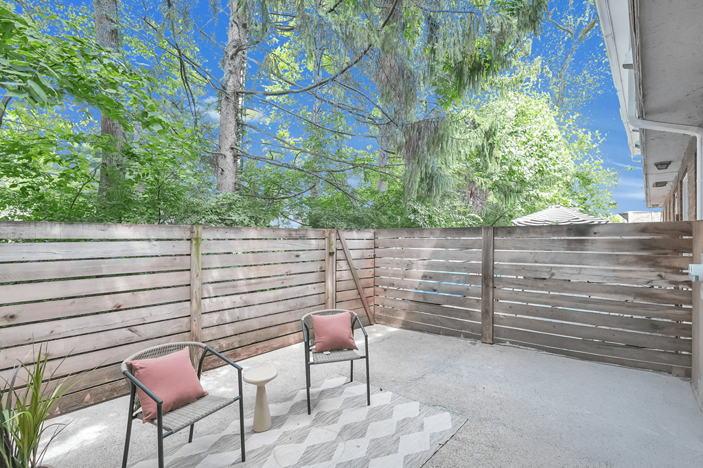 Two chairs are placed on a patio with a wooden fence and trees in the background.