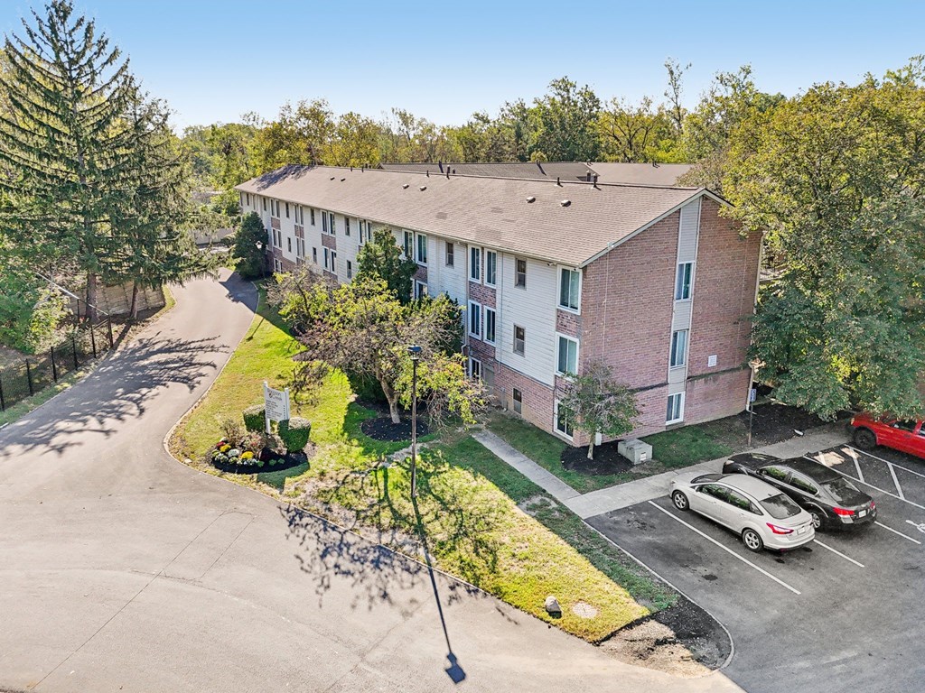 A red car is parked in a parking lot in front of a building.