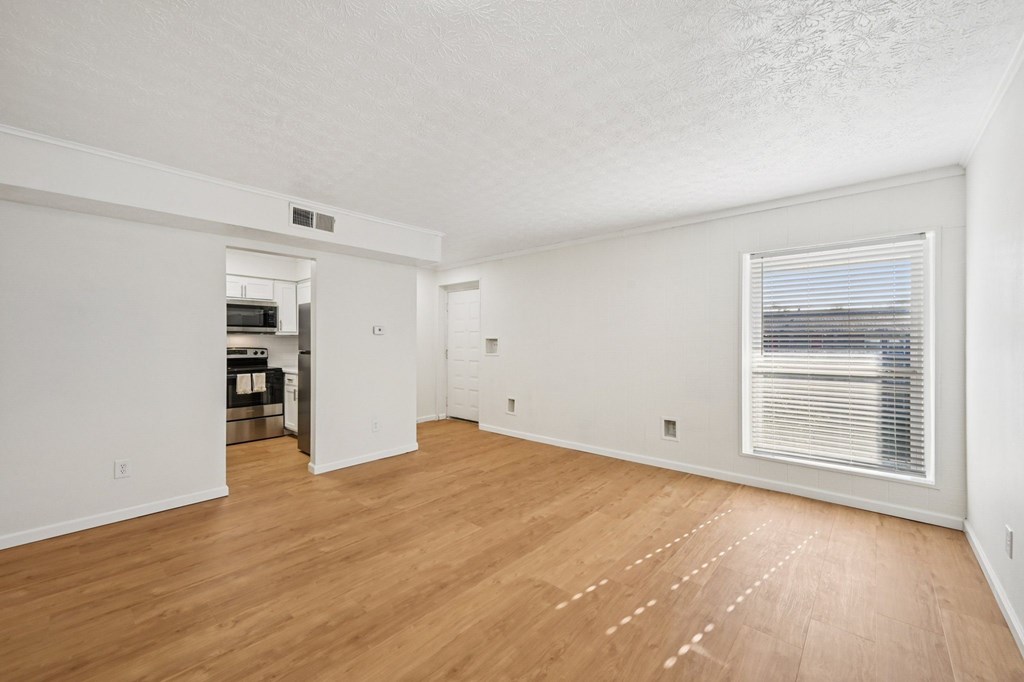 A large empty room with wooden floors and a window with blinds.