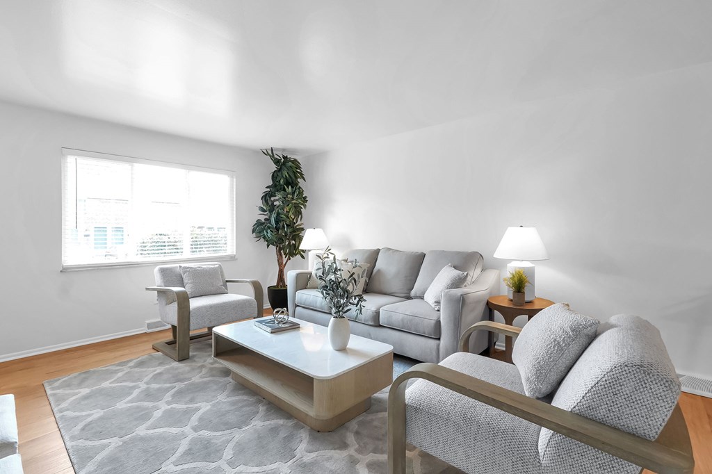 A living room with a grey couch, a grey chair, a coffee table, and a plant.