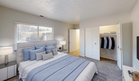 A bedroom with a large bed and a closet with clothes hanging.