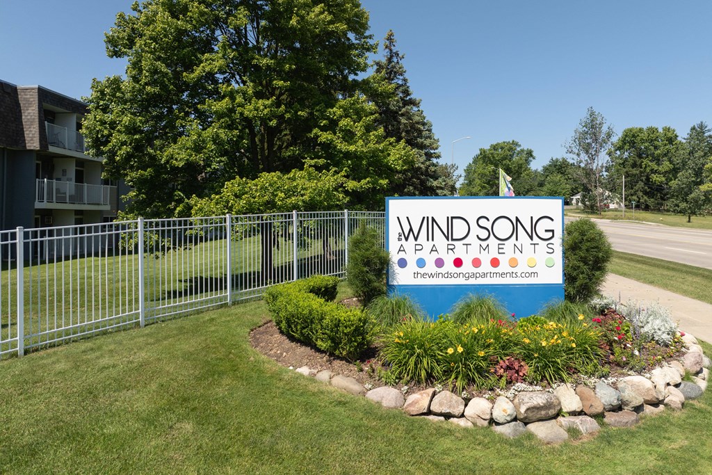a sign for wind song apartments in front of a fence