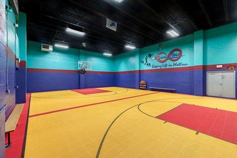 a basketball court in a gym with a blue wall and a red and yellow floor