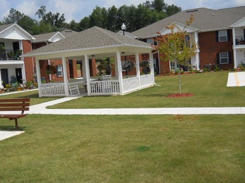 A gazebo is in the middle of a grassy area in front of apartment buildings.