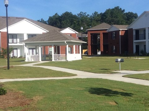 A white building with a porch is in the middle of a grassy area.