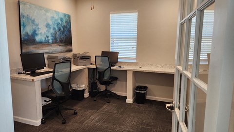 an office with three desks with computers and a painting on the wall