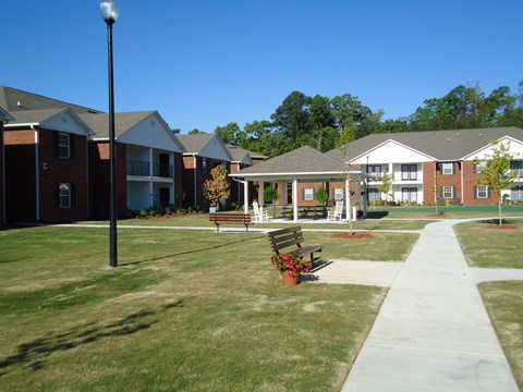 A grassy area with benches and a pathway in front of apartment buildings.