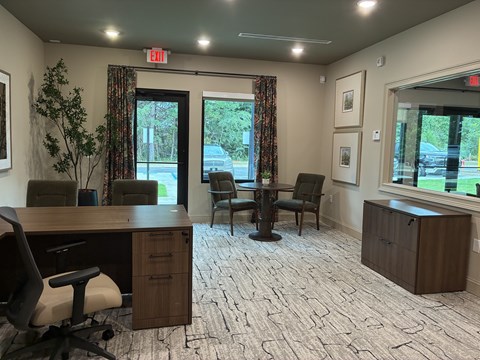 A conference room with a desk, chairs, and a view of the parking lot outside.