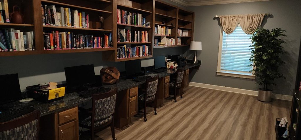 A room with a desk, chairs, and a bookshelf filled with books.