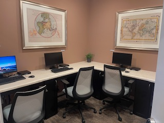 A room with a desk and chairs and two maps on the wall.