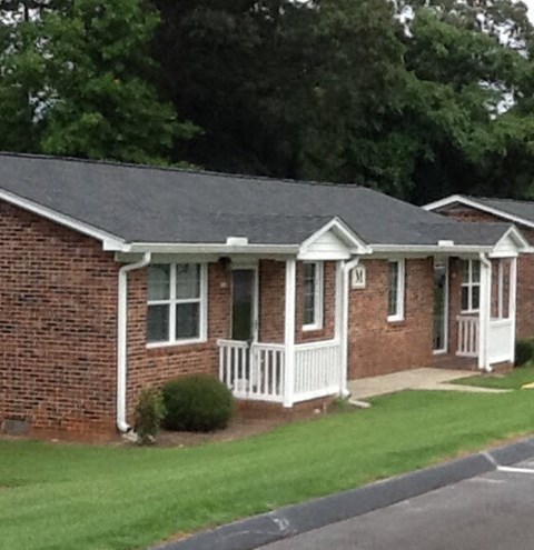 a small brick house with a porch and a lawn