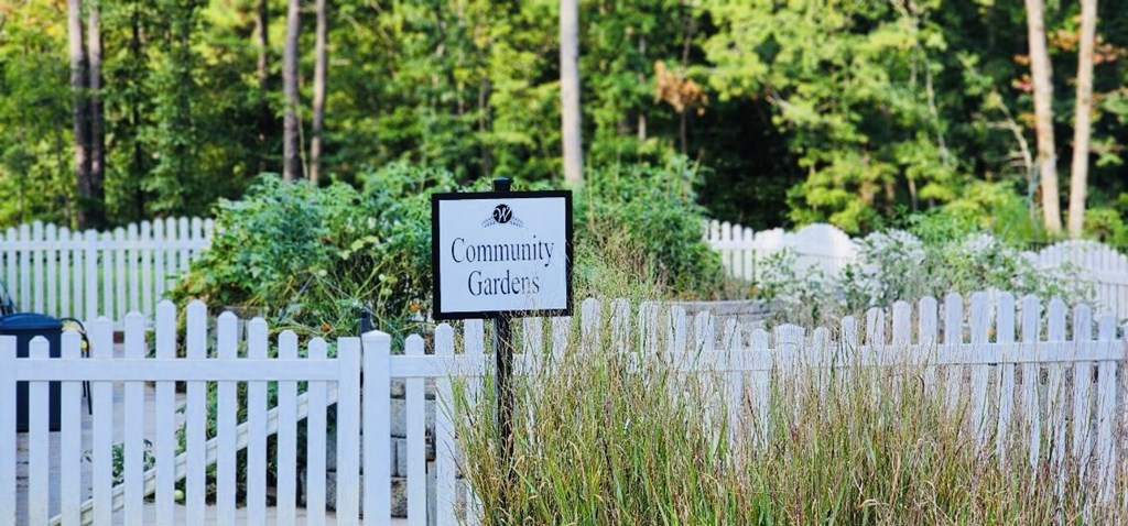 A sign that says Community Gardens stands in front of a white picket fence.