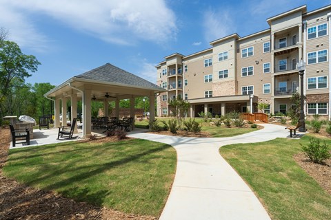 A gazebo is surrounded by a grassy area in front of apartment buildings.