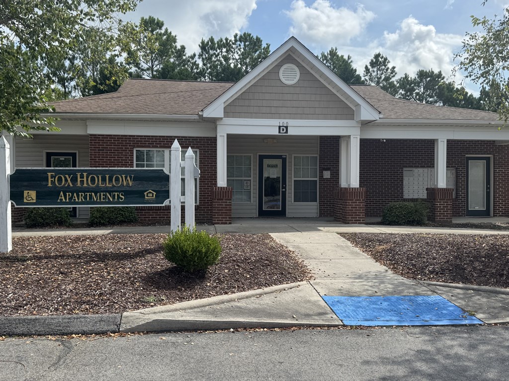 The front of the Fox Hollow Apartments building is shown with a blue mat on the sidewalk.