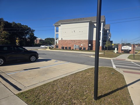 A black car is parked in a parking lot in front of a building with a sign that says "Pine.".