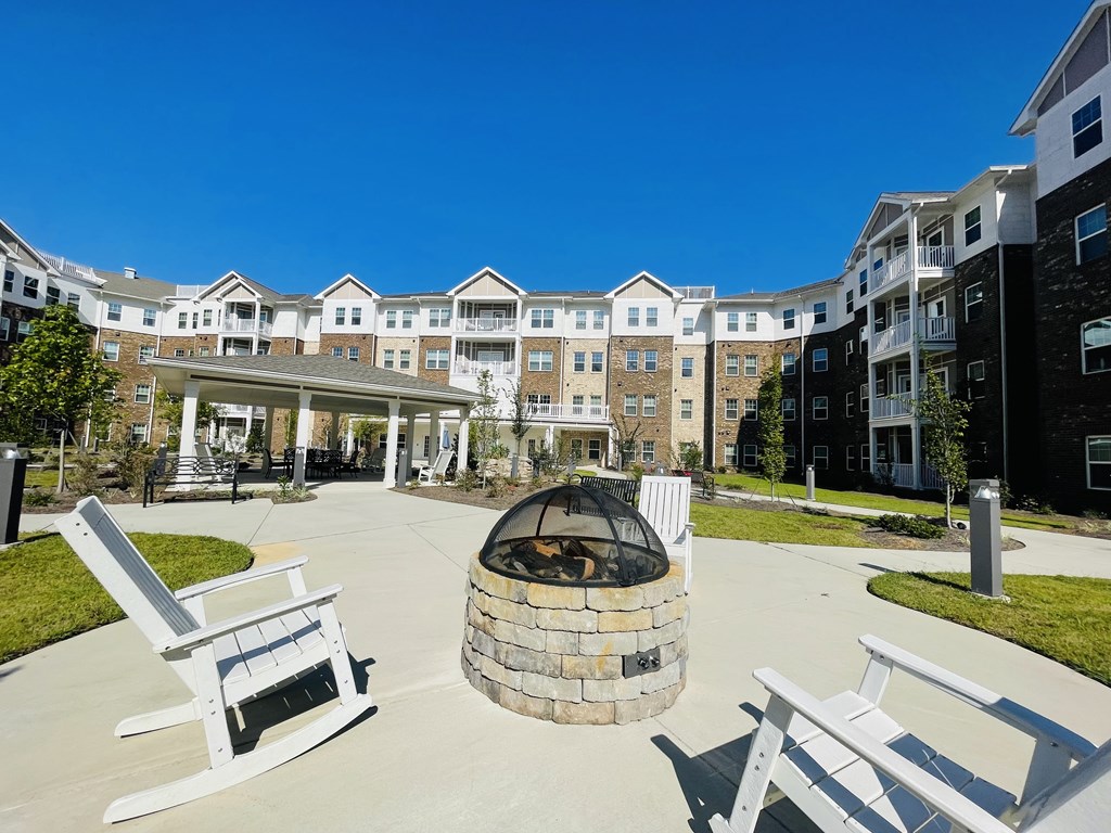 A fire pit sits in the middle of a courtyard with white chairs around it.