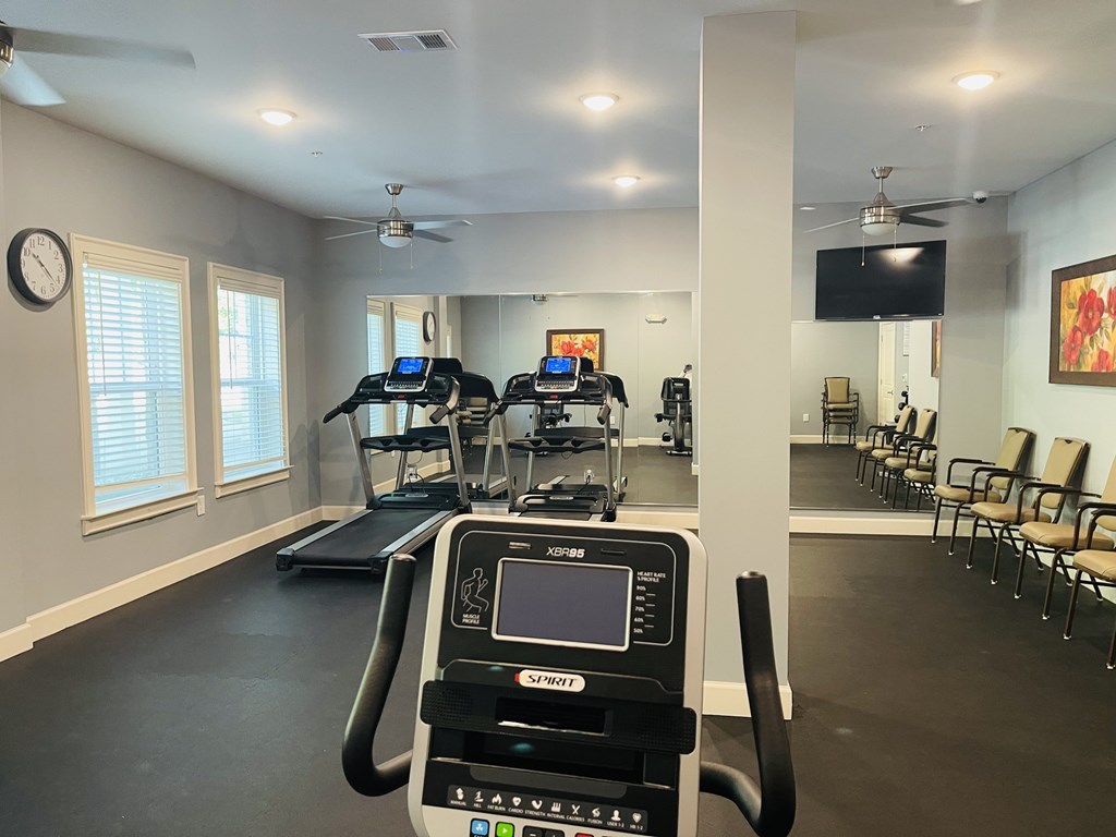 A gym with treadmills, elliptical machines, and a television.