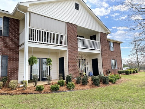 the front of a brick house with a porch and a balcony