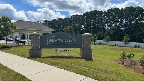 A sign for Abbington Village stands in front of a building and trees.